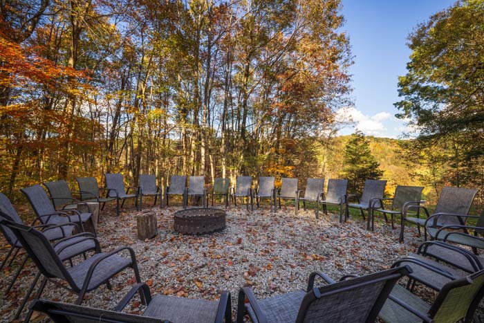 Large fire pit circle with lounge chairs in the fall woods at High Point Lodge