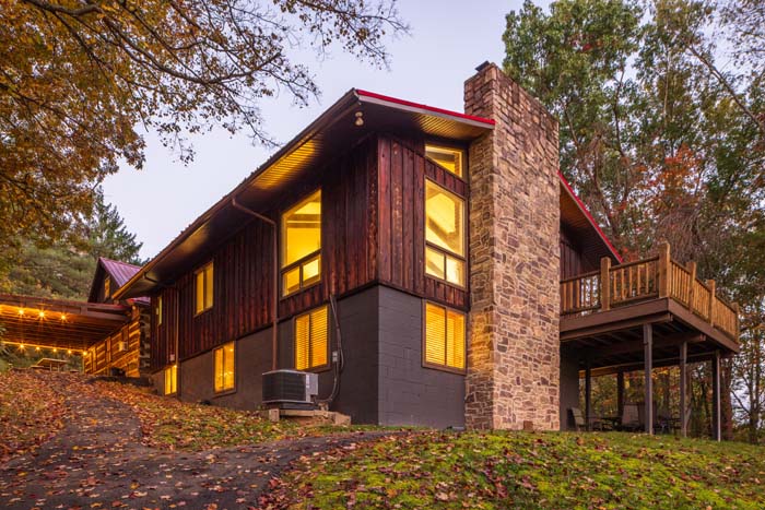 Two story lodge wing with stone chimney lit at dusk at High Point Lodge