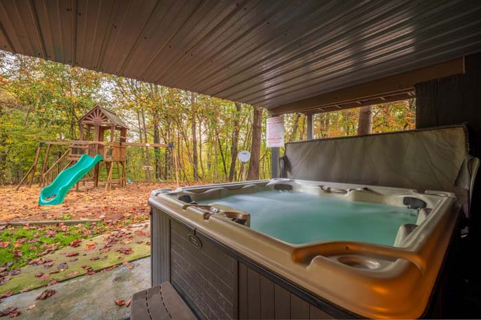 Covered hot tub with view of the playset and woods at High Point Lodge