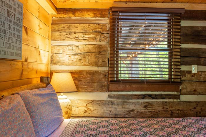 Bed and lamp against the hand hewn log wall at High Point Lodge