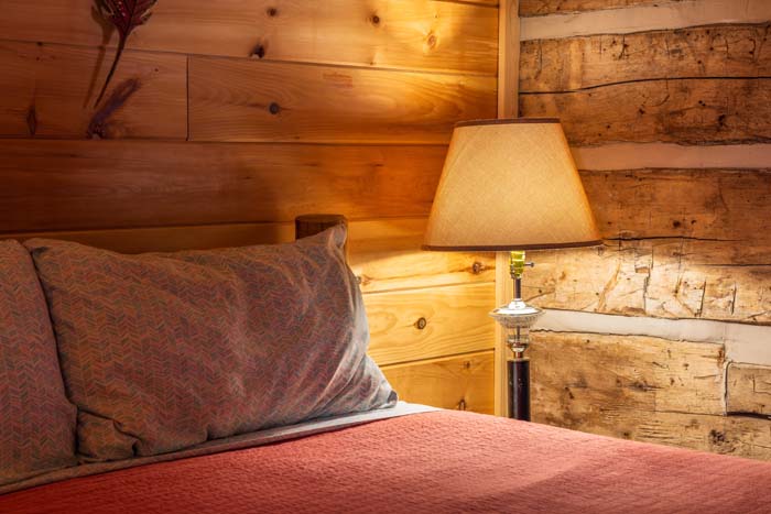Bed with red quilt and lamp beside the log wall at High Point Lodge